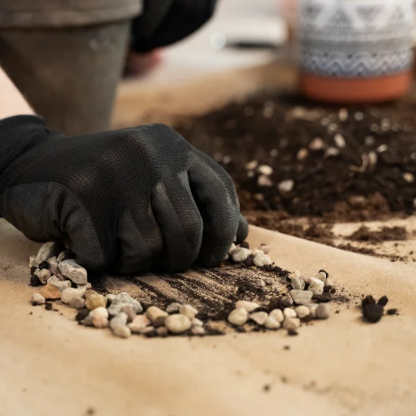 Une personne en gants utilise une pelle pour étendre de la terre sur du gazon existant.